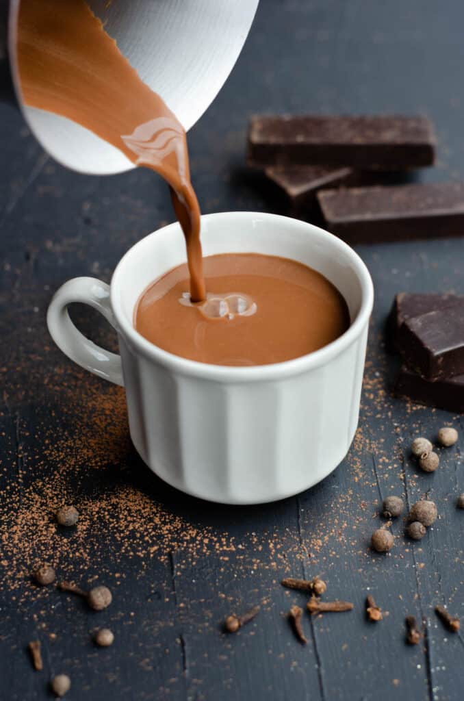 a cup of spiced hot chocolate being poured from the pot into the cup