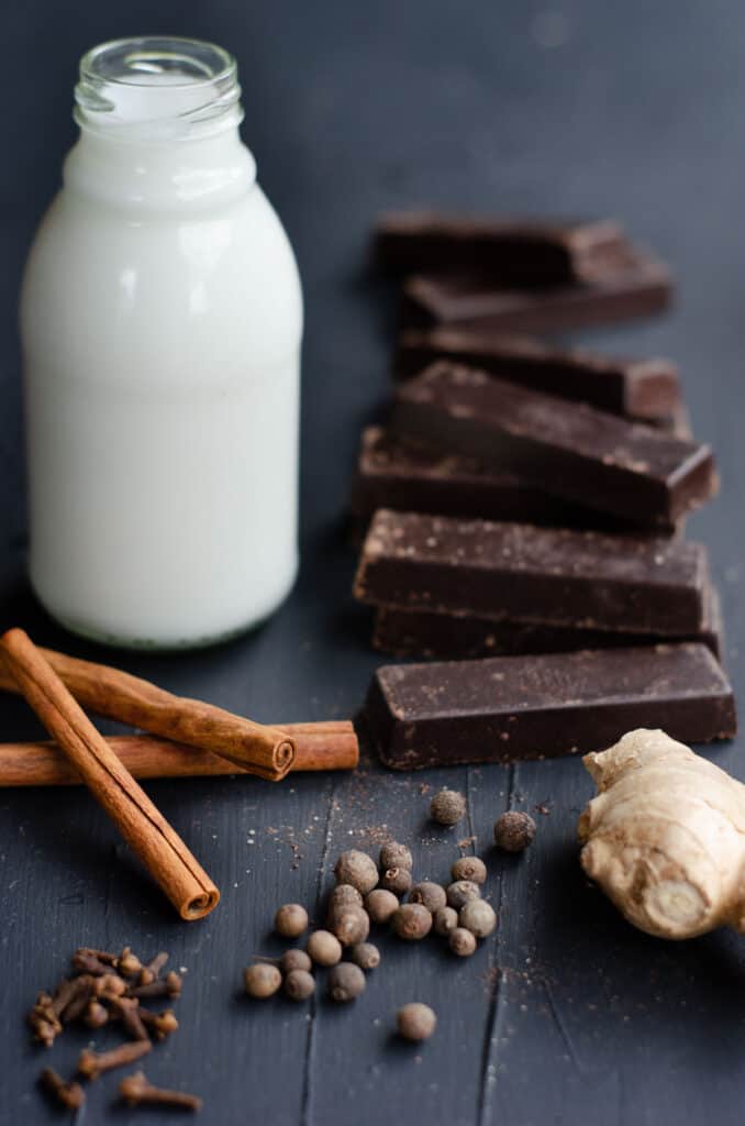 ingredients to make spiced hot chocolate: coconut milk, chocolate bars, fresh ginger, cinnamon sticks, whole allspice and cloves