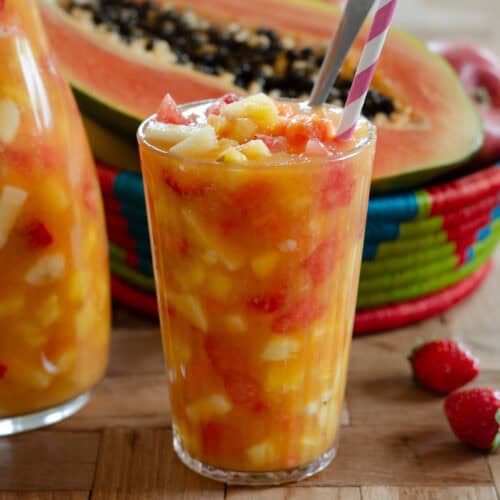 glass of salpicon colombian fruit cocktail, with a pitcher of salpicon and a traditional basket with papaya and strawberries